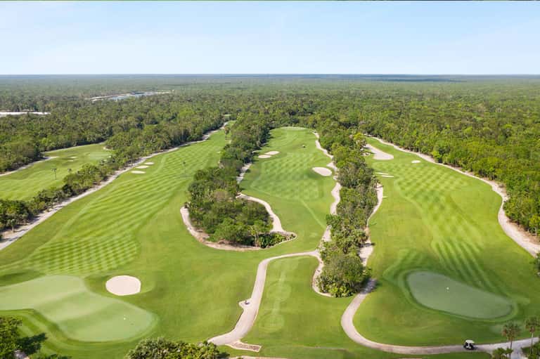 Aerial view of manicured golf course with white sand bunkers, fairways, and forest surrounding