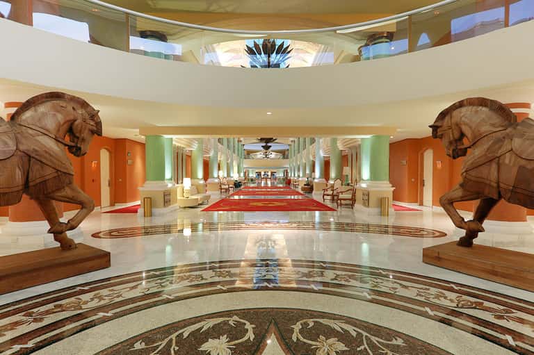 Luxury hotel lobby with grand wooden elephant sculptures, orange and green columns, and elegant flooring
