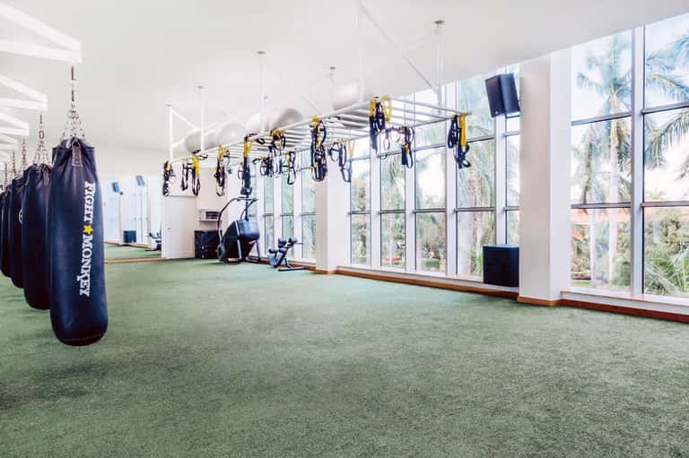 Modern fitness center with suspended bikes and punching bags, large windows overlooking palms