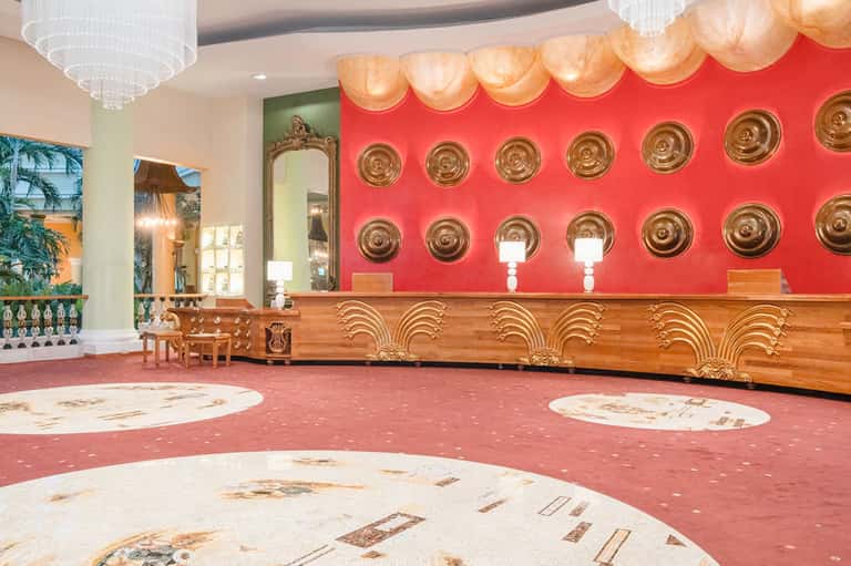 Elegant hotel lobby with red accent wall, gold decorative plates, and wooden reception desk
