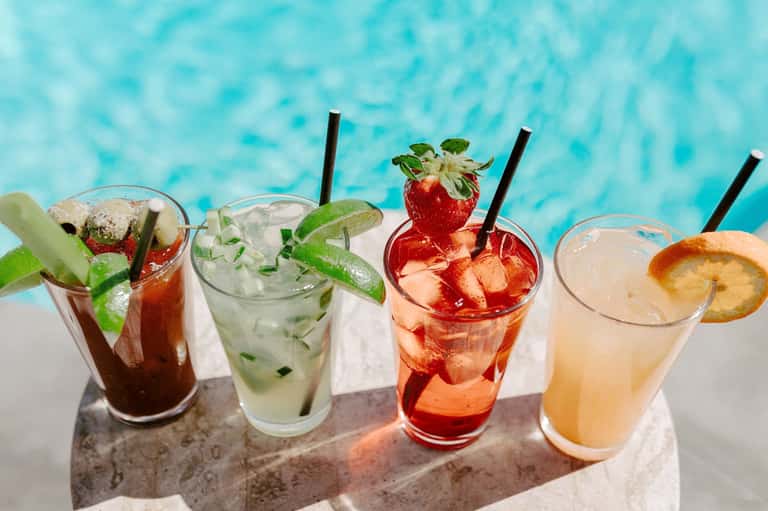 Colorful cocktails with fresh fruit and herbs displayed by turquoise poolside