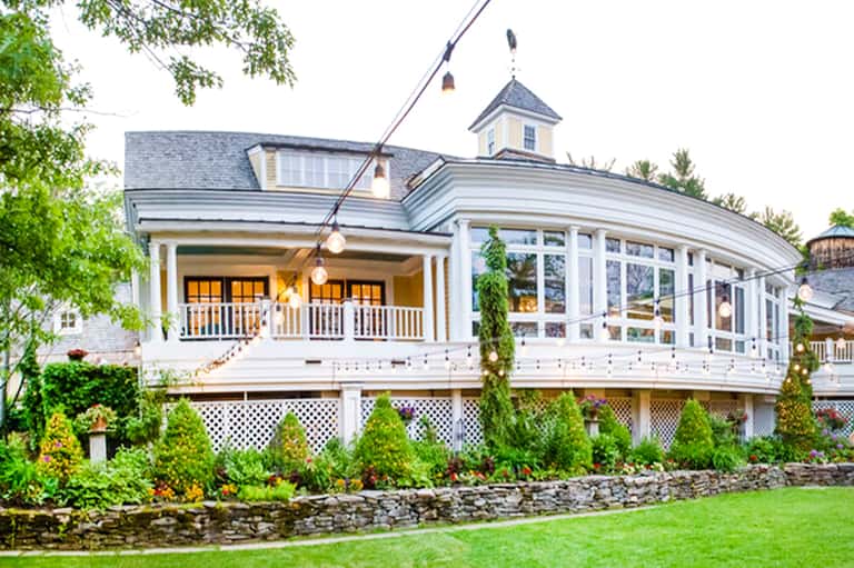 Elegant New England coastal home with wraparound porch, yellow doors, white railings, and manicured gardens
