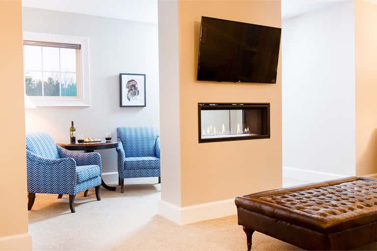 Upscale hotel suite with fireplace, mounted TV, blue patterned chairs, and peach accent wall