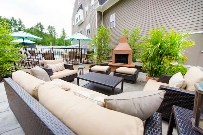 Contemporary outdoor patio with curved cream seating, fireplace, and lush greenery