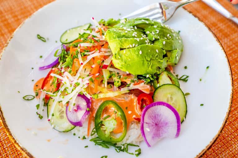 Colorful gourmet salad with avocado, sesame seeds, fresh vegetables on white plate
