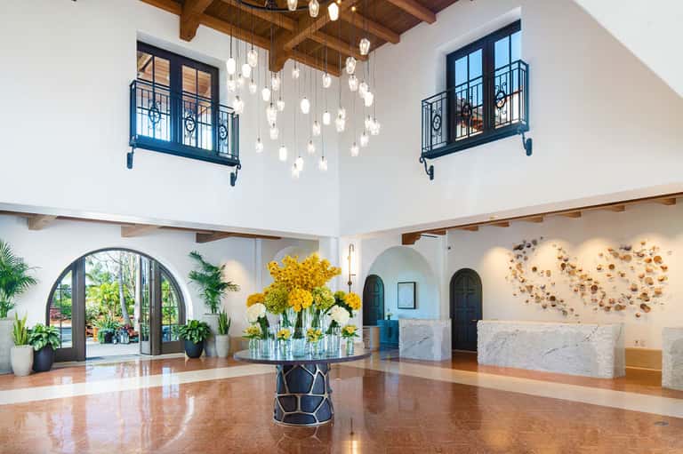 Luxurious hotel lobby with high ceilings, hanging pendant lights, marble elements, and yellow flowers