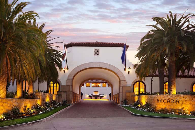Illuminated Mediterranean-style resort entrance with arches, palm trees, and fountain at dusk