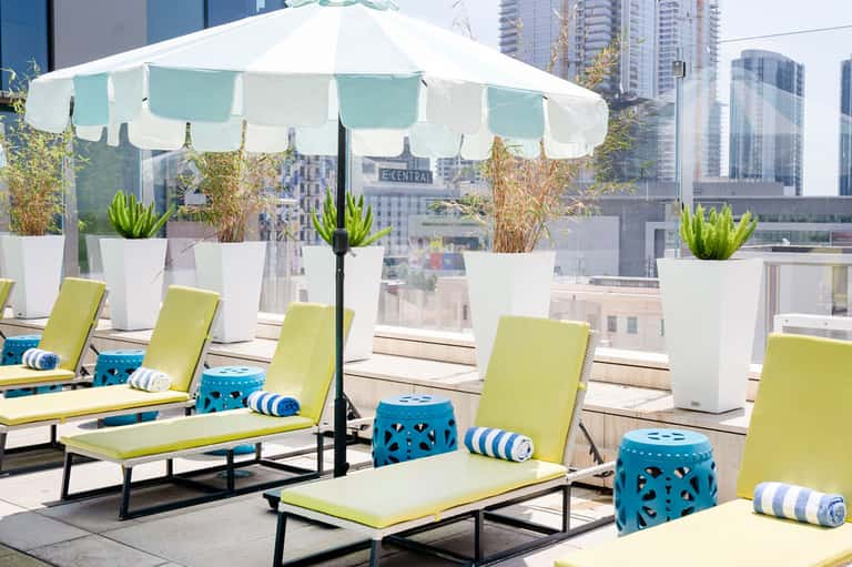 Rooftop lounge with lime green loungers, white umbrella, potted plants, and city skyline
