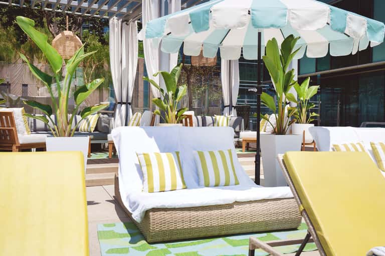 Modern resort loungers with yellow cushions and striped pillows under a turquoise and white canopy