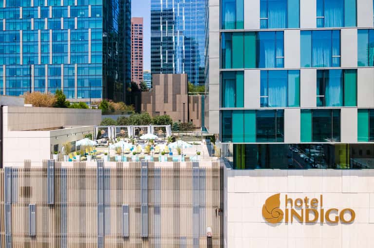 Hotel Indigo rooftop pool area with yellow lounge chairs, city skyline, and modern building architecture
