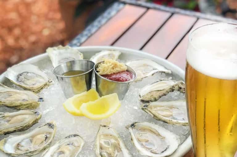 Platter of fresh oysters on ice with lemon wedges, condiments, and beer