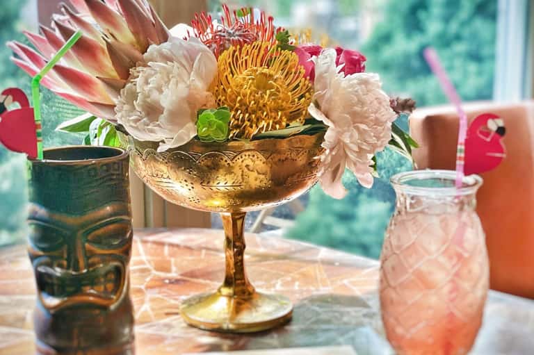 Colorful floral arrangement in gold bowl with white peonies, red proteas, and yellow chrysanthemums