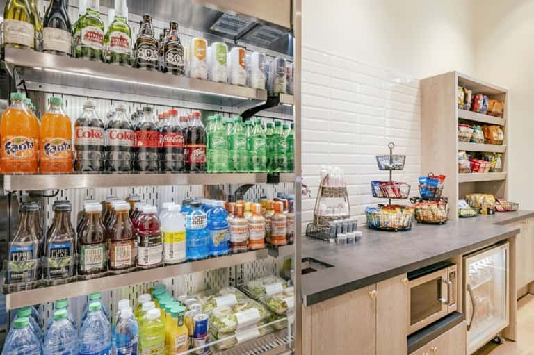 Hotel beverage station with stocked shelves of beverages, snacks, and amenities on granite counter