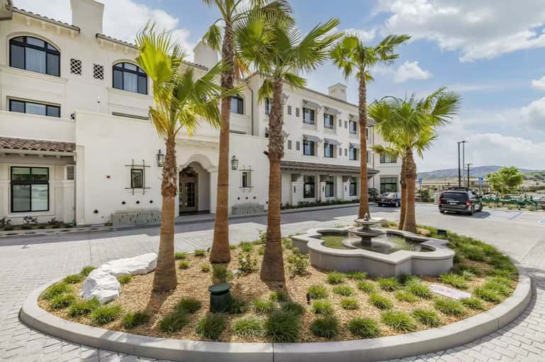 White Spanish-style hotel exterior with palm trees, arched entrance, and fountain courtyard