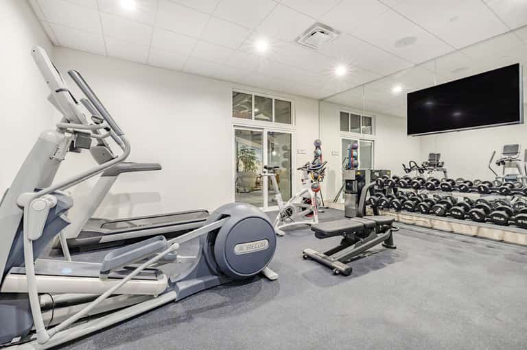 Modern fitness center with cardio equipment, weights, and TV monitor