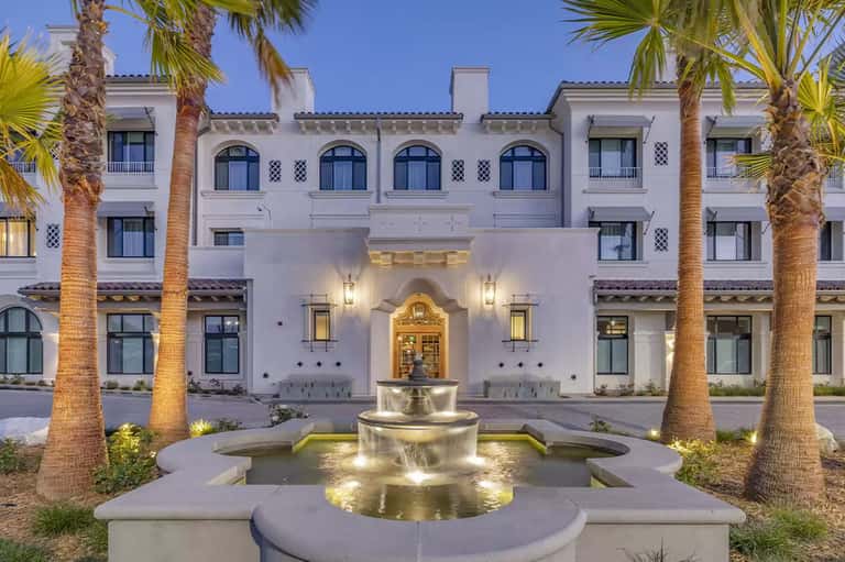 Illuminated Mediterranean-style white resort building courtyard with fountain at dusk surrounded by palms