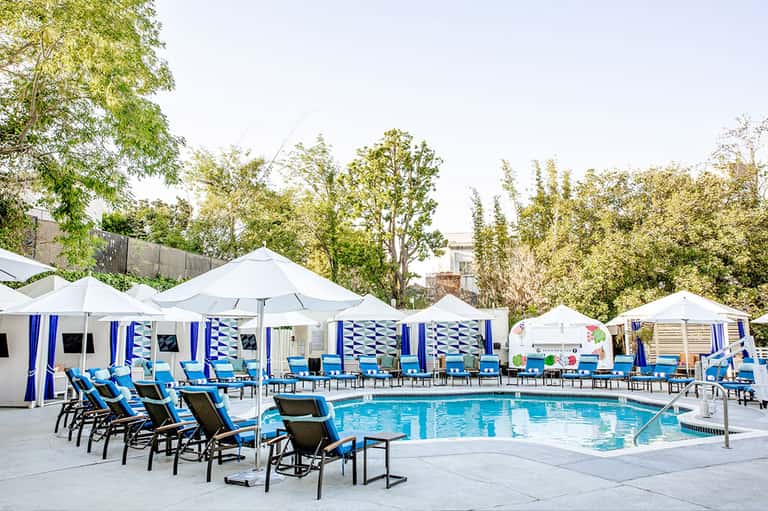 Resort pool with striped cabanas, white umbrellas, and green trees surrounding patio area