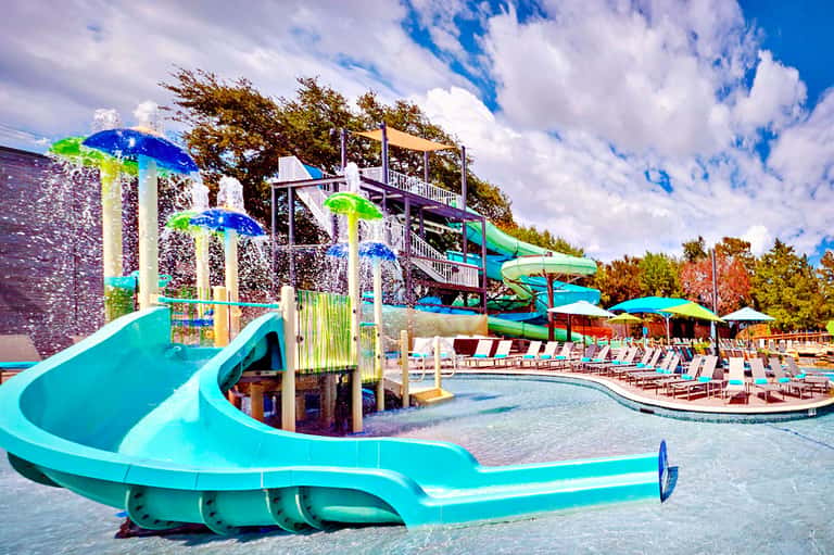 Colorful water slides and splash pad with lounge chairs at outdoor resort pool area