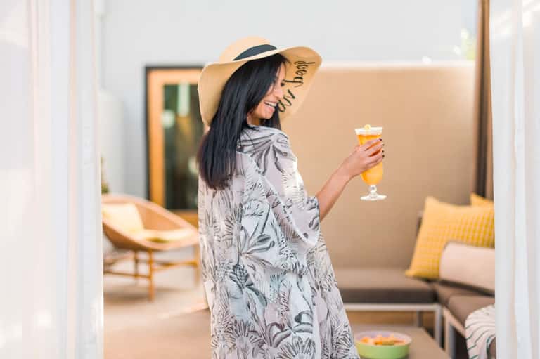 Woman in straw hat holding beverage on sunny resort terrace with lounge seating