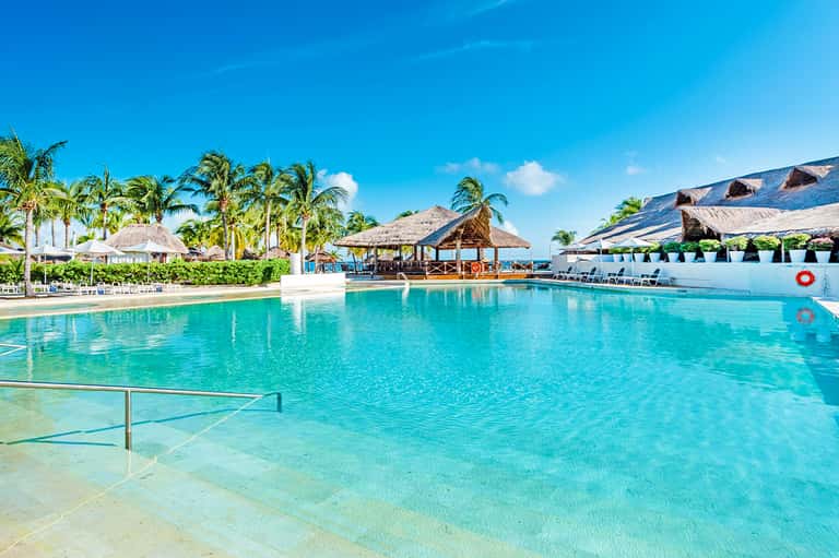 Resort lagoon pool with thatched-roof bungalows, palm trees, and tropical setting