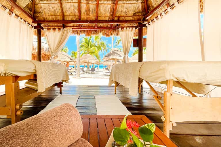 Beachfront spa or lounge pavilion with thatched roof, white curtains, and ocean view beyond