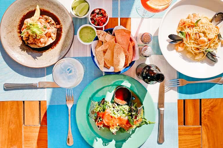 Colorful seafood dishes on blue tablecloth with cocktails and appetizers on outdoor dining table