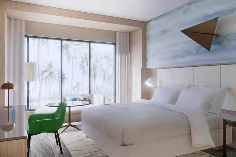 Modern hotel bedroom with white bedding, green accent chair, ocean view, and beach-inspired wall art