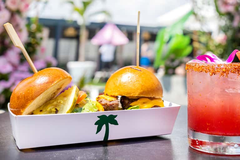 Gourmet burgers and tropical cocktails served poolside with pink flowers in background