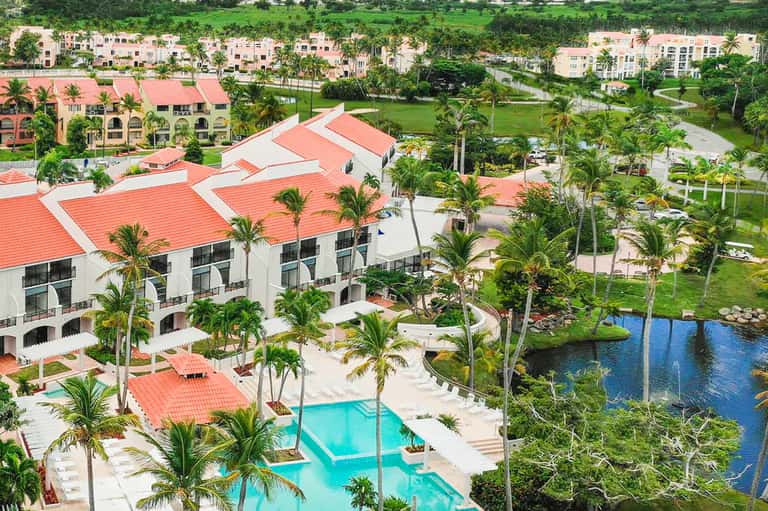 Resort clubhouse with coral roof overlooking turquoise pool, landscaped grounds, and lake
