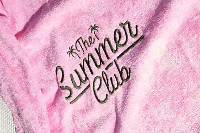 Pink towel embroidered with 'That Summer Club' text with palm tree designs
