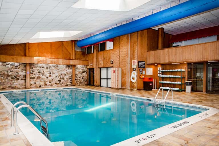 Indoor lap pool with wooden beams, white ceiling, and stone accent walls