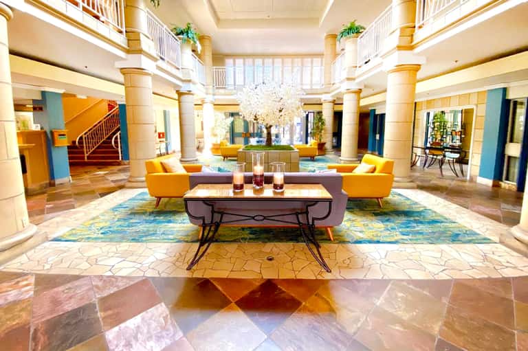 Grand hotel lobby with colorful floor tiles, yellow armchairs, and crystal chandelier under high ceiling