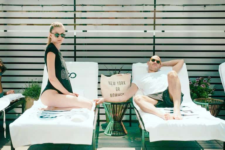 Two guests relaxing on white lounge chairs against a striped green and white backdrop