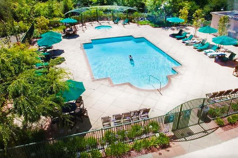 Resort pool surrounded by turquoise umbrellas, lounge chairs, and lush green landscaping