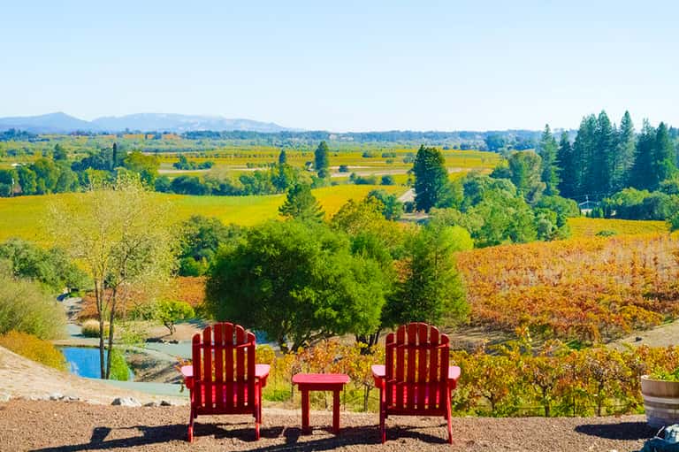 Red Adirondack chairs overlooking vineyards and rolling hills landscape