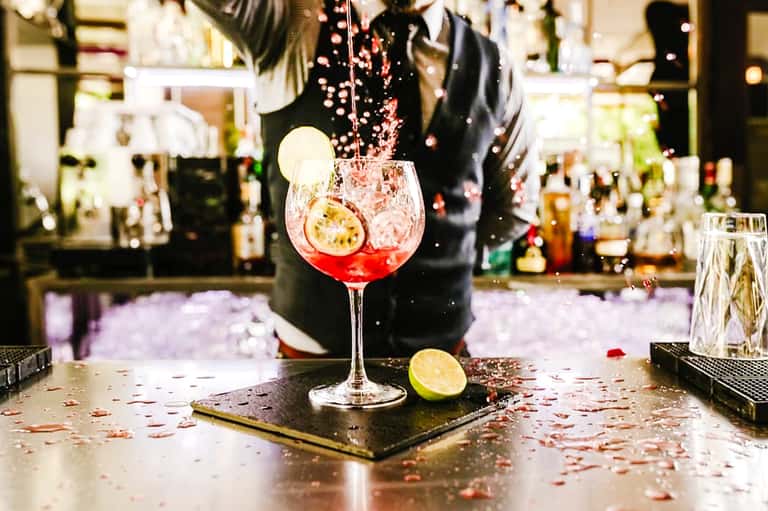 Bartender pouring red cocktail into glass at hotel bar with bottle display