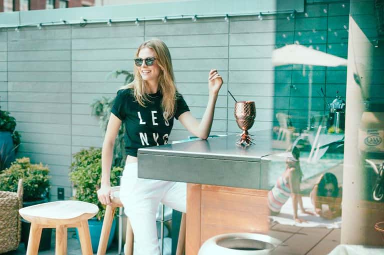 Woman enjoying tropical drink at outdoor rooftop bar with green glass walls and potted plants