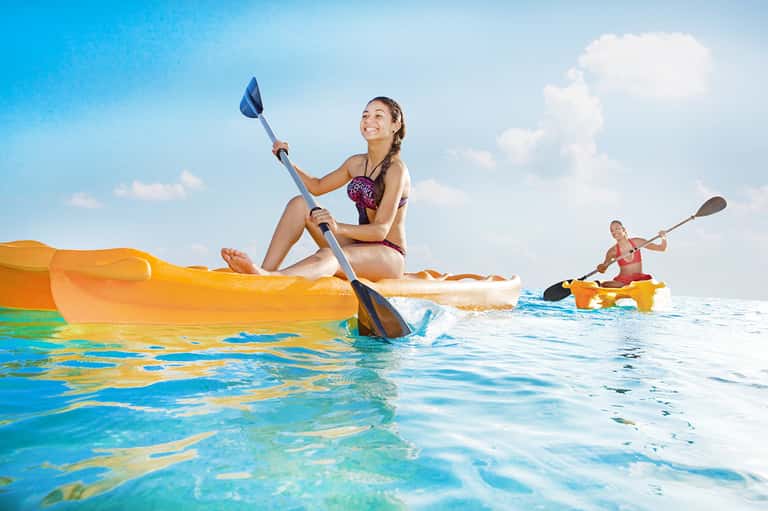 Two women kayaking in turquoise ocean water with yellow kayaks on sunny day