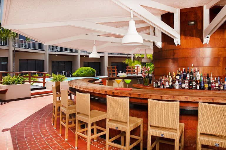 Outdoor bar with wooden counter, wicker seating, and canvas sail shade