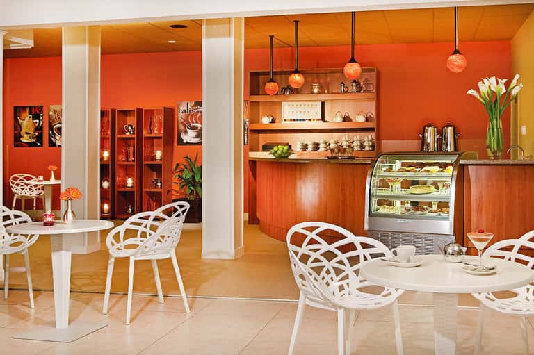 Bright orange café interior with white geometric chairs, wooden shelving, and pendant lighting