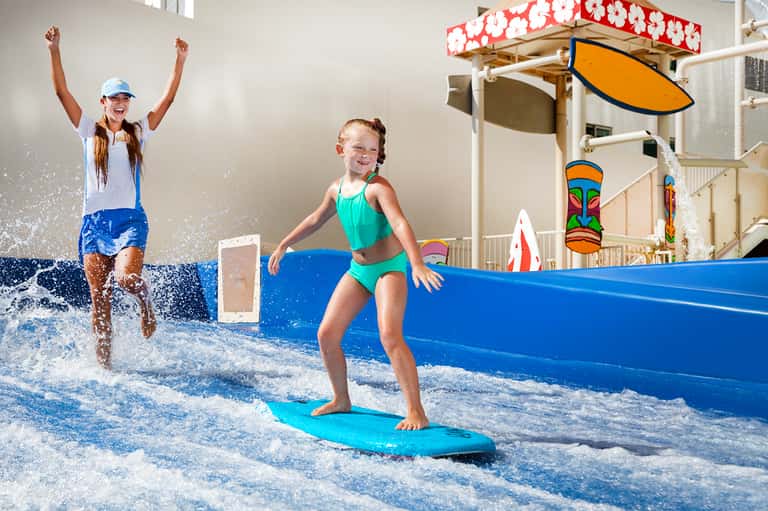 Children learning to surf in indoor wave pool with professional instructor