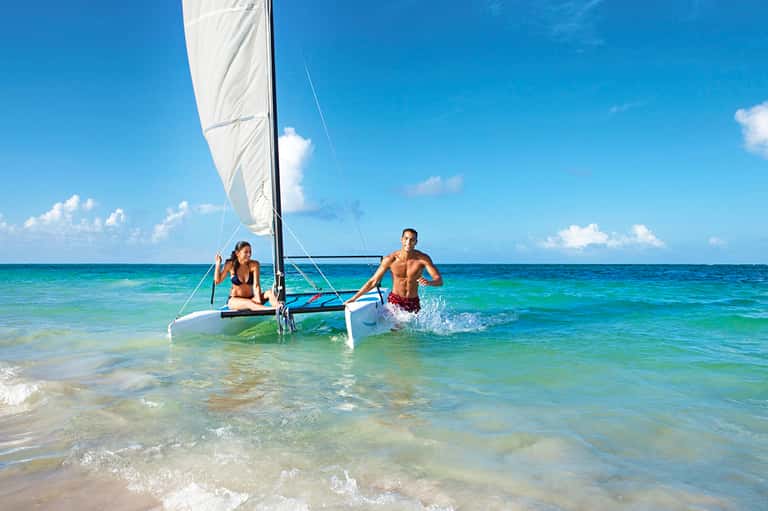 Couple with sailboat in crystal-clear turquoise tropical ocean water