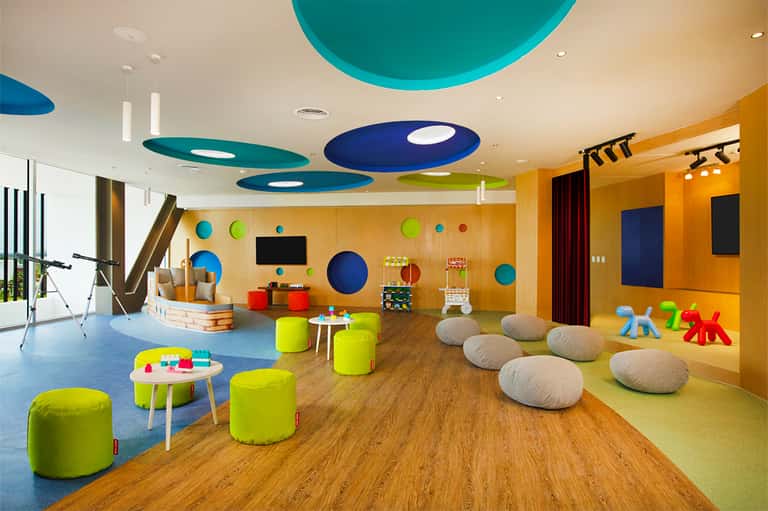 Colorful children's playroom with bright yellow walls, blue ceiling features, soft seating, and interactive toys