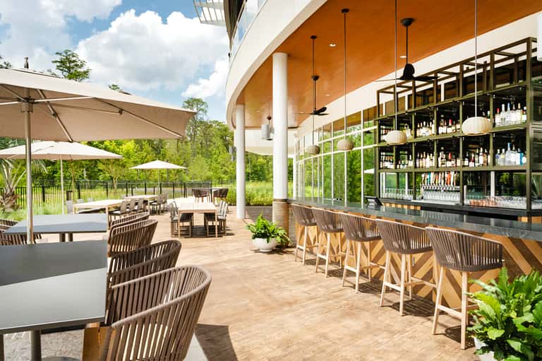 Modern outdoor bar and lounge area with orange ceiling, seating, and lush tropical surroundings