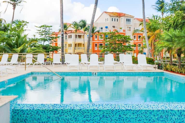 Resort pool with white lounge chairs, colorful buildings, and palm trees