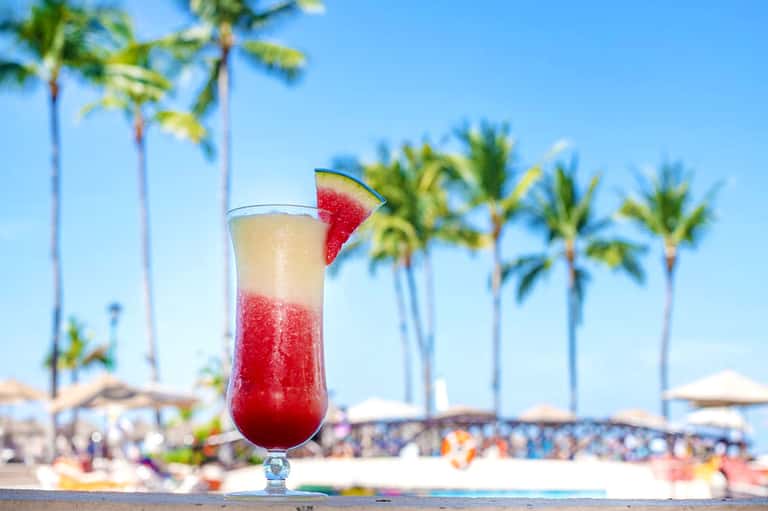 Refreshing red cocktail with watermelon garnish on tropical beach with palm trees