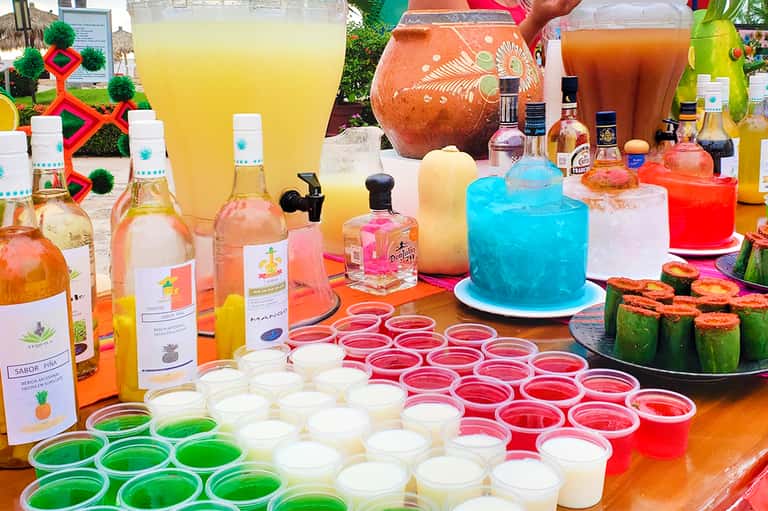 Colorful tropical drink bar display with bottles, juices, cakes, and vibrant beverages