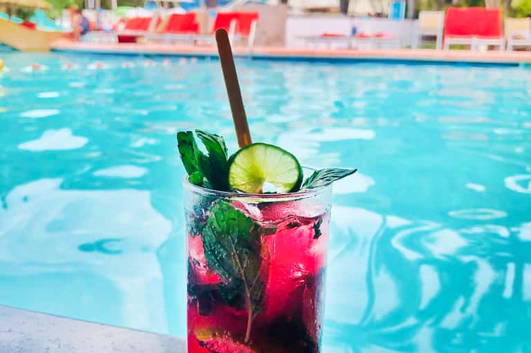 Colorful cocktail with lime and mint garnish on pool deck edge overlooking resort swimming pool
