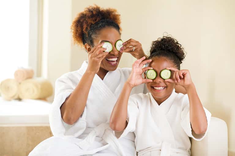 Two women in spa robes laughing with cucumber slices over their eyes