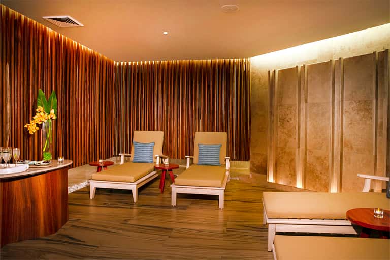 Spa relaxation room with gold loungers, blue accent pillows, dramatic curtains, and warm ambient lighting
